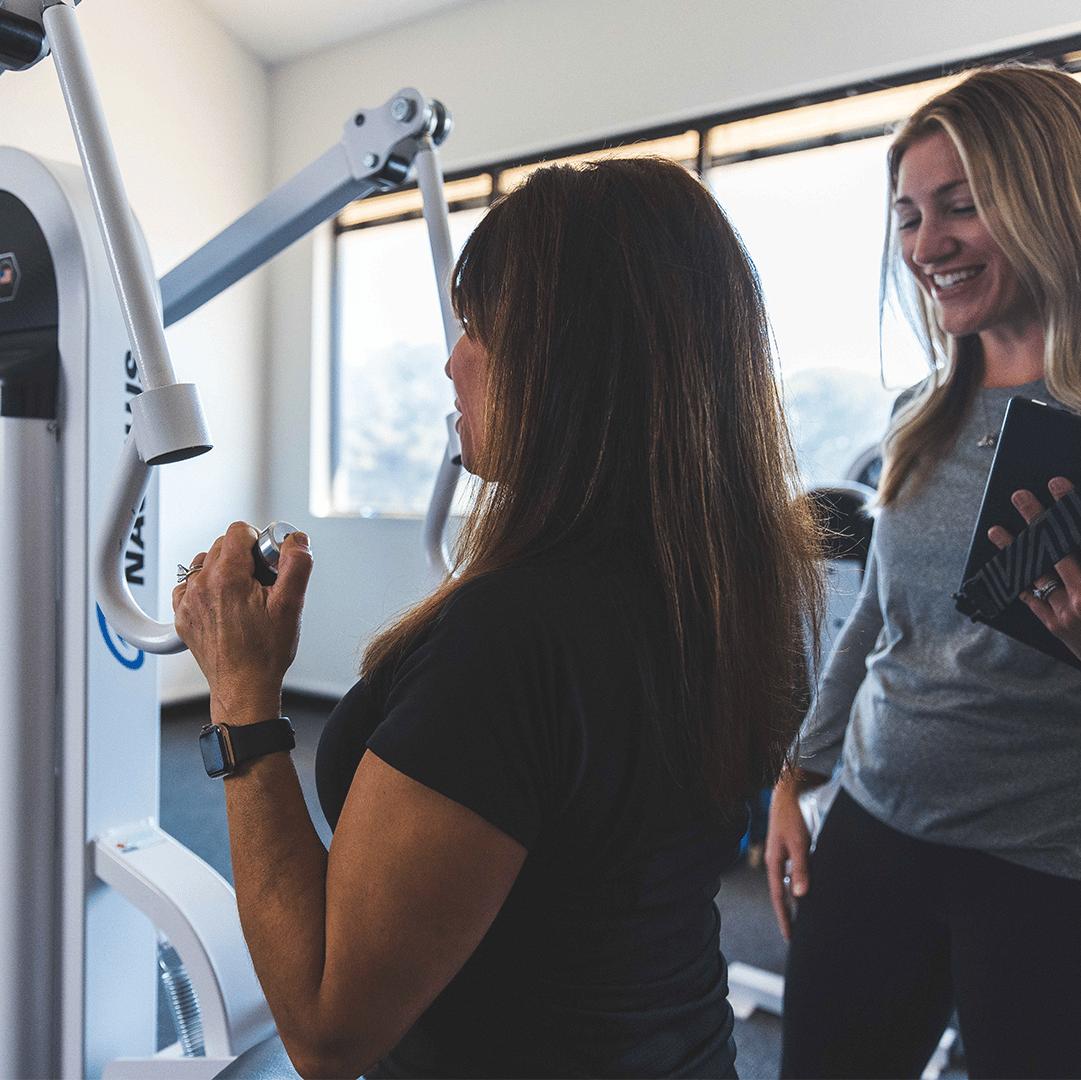 A personal trainer helps a woman lift weights with full range of motion