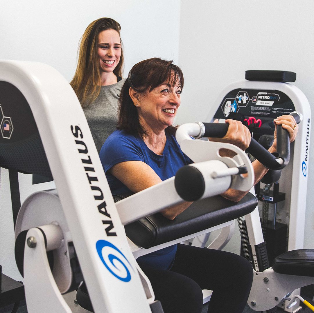 A woman working with a personal trainer on a preacher curl machine