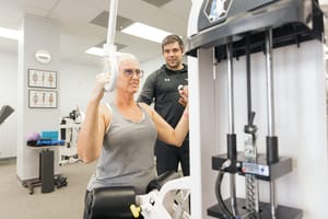 Determined woman working out on a resistance machine with guidance from a personal trainer.