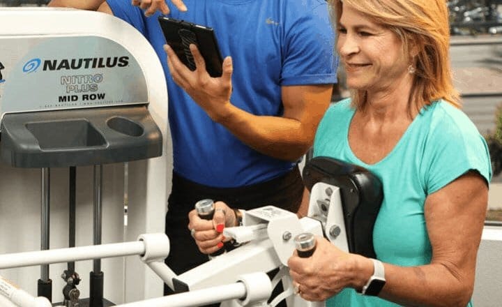 female client strength training on a nautilus machine with a personal trainer