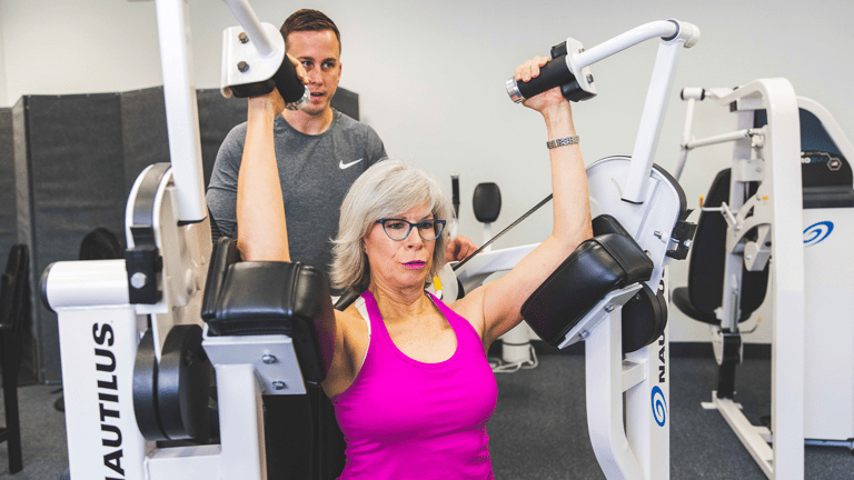 Image of a female member being coached by a trainer on the triceps machine