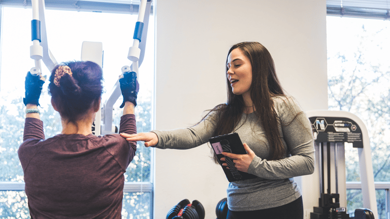 Image of Valeria coaching a member on the Lat Pulldown machine