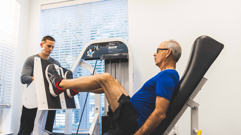 A trainer helps a man on the leg press machine