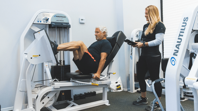 Image of a man being trained on a leg press by a female trainer