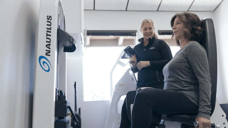 A trainer at The Perfect Workout helping a woman on the adduction/abduction machine