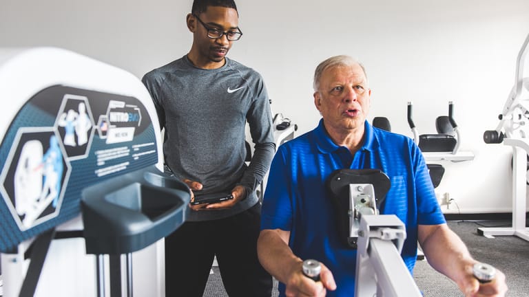 A trainer helps a man perform the mid row exercise