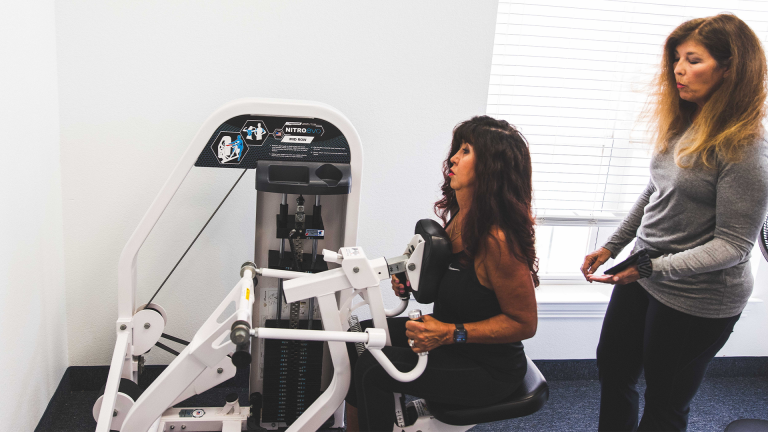 A trainer coaching a woman on the compound row machine