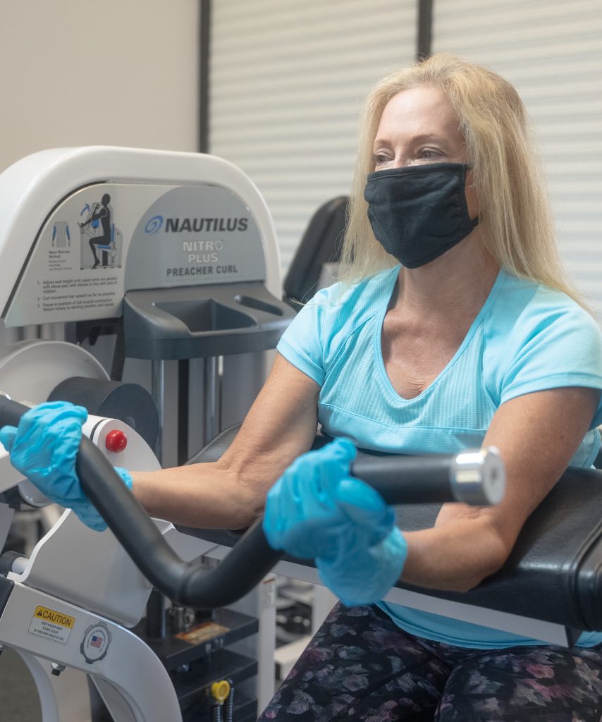 Client in mask in gloves safely working out in medical fitness facility during a personal training session