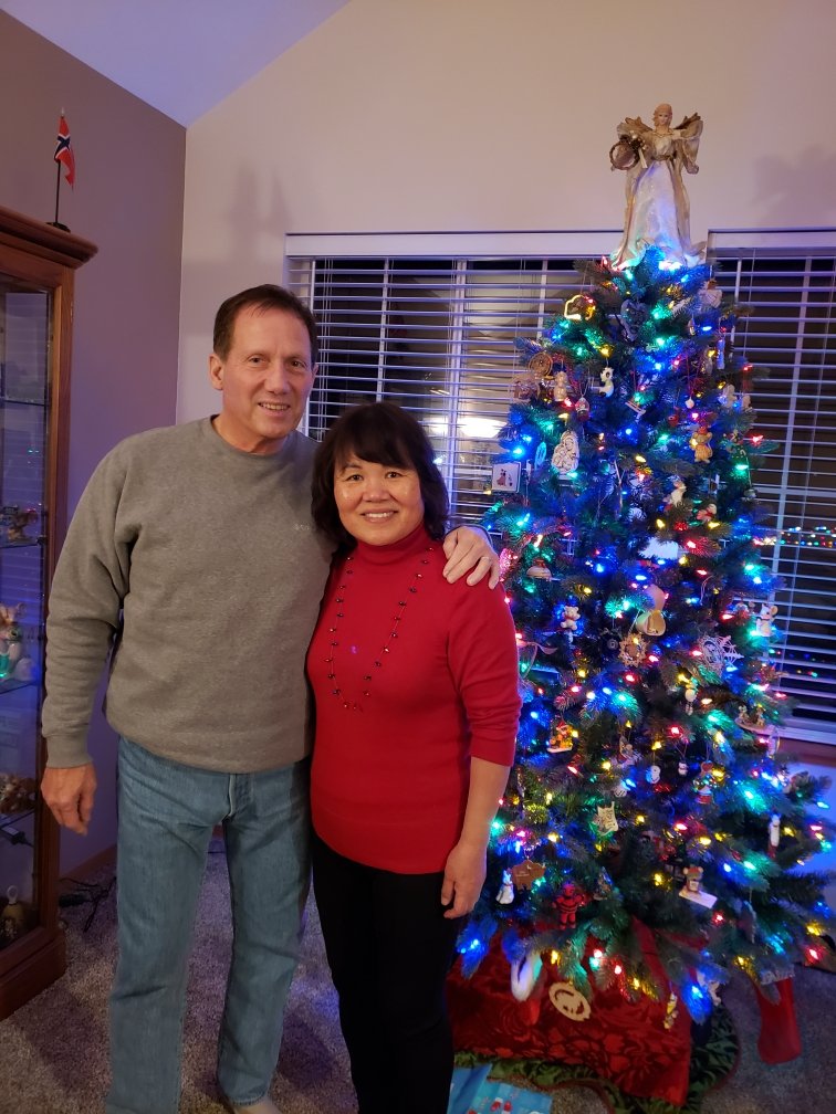 husband and wife standing in front of a christmas tree together