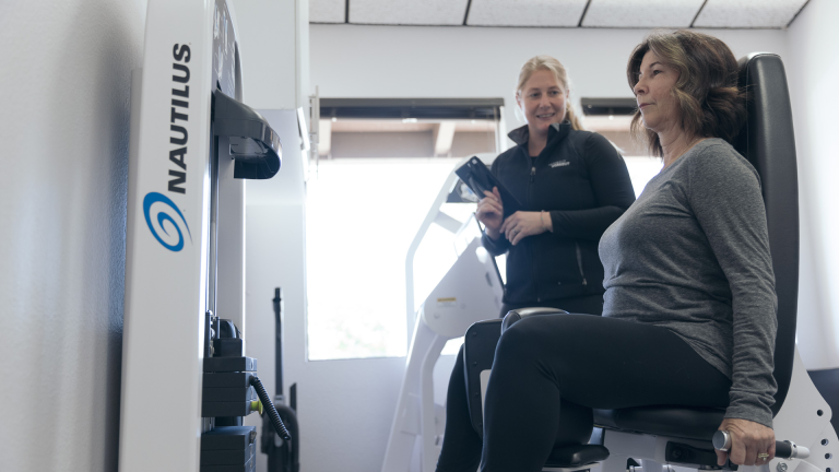 A trainer helps a woman on the Adduction/Abduction machine at The Perfect Workout