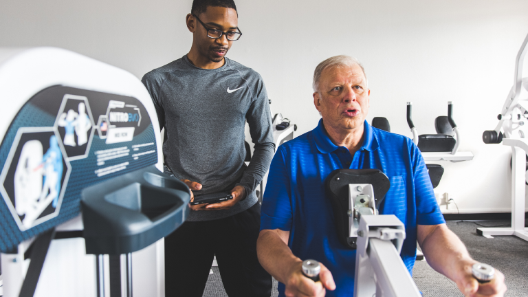 A trainer helps a man perform the mid row exercise