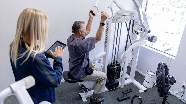 A trainer directs a man on proper form on the lat pulldown machine